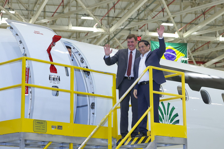 Thủ tướng Phạm Minh Chính và lãnh đạo Embraer vẫy tay chào sau khi rời buồng lái chiếc Embraer - Ảnh: NHẬT BẮC