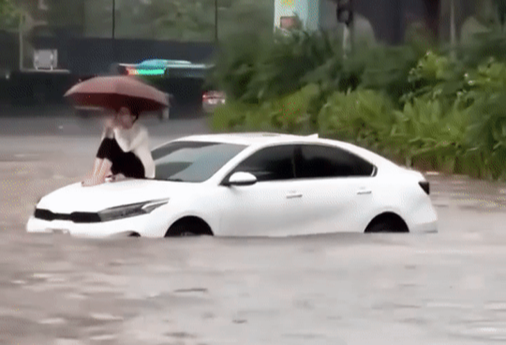Cảnh chị C. ngồi trên nóc ô tô giữa đường ngập nước được người đi đường ghi lại - Ảnh: Mạng xã hội  