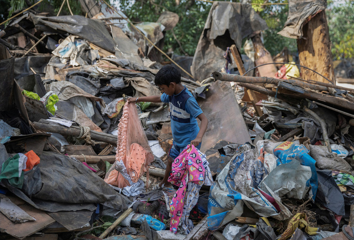 Ishant Kumar, 10 tuổi, từng sống tại khu ổ chuột Janta Camp, đang nhặt nhạnh quần áo của gia đình mình từ ngôi nhà cũ vừa bị phá hủy - Ảnh: REUTERS