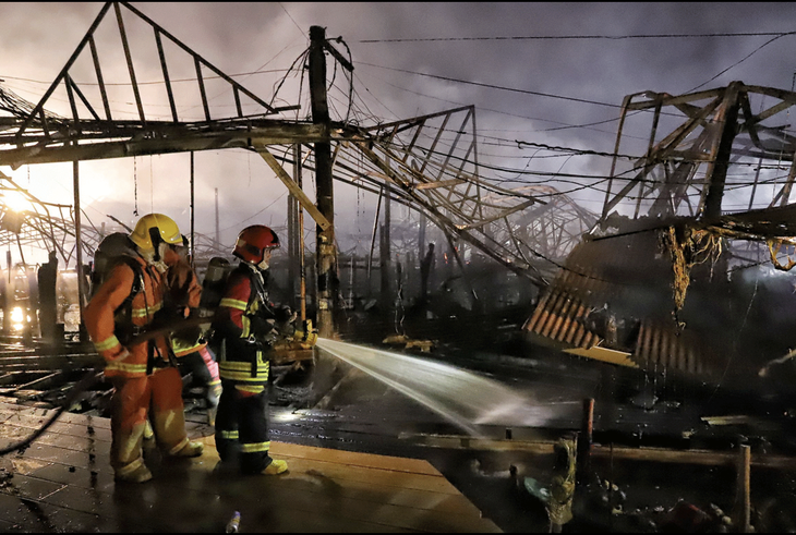 Lực lượng cứu hỏa tiếp tục phun nước lên các mái nhà đã cháy nham nhở để ngăn ngọn lửa bùng phát trở lại ở chợ nổi Pattaya - Ảnh: BANGKOK POST