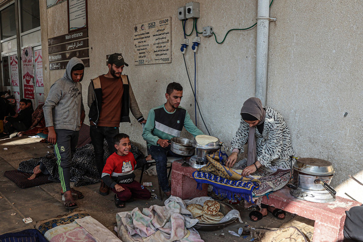Thanh niên quây quanh người phụ nữ đang chuẩn bị thức ăn tại khu trại dành cho người Palestine di tản bên ngoài Bệnh viện Châu Âu ở Khan Yunis, ngày 31-12-2023 - Ảnh: AFP