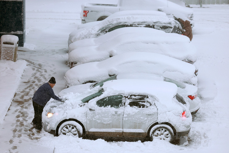 Một người đàn ông dọn lớp tuyết dày trên xe ô tô khi cơn bão tuyết quét qua bang Iowa vào ngày 9-1 - Ảnh: CNN