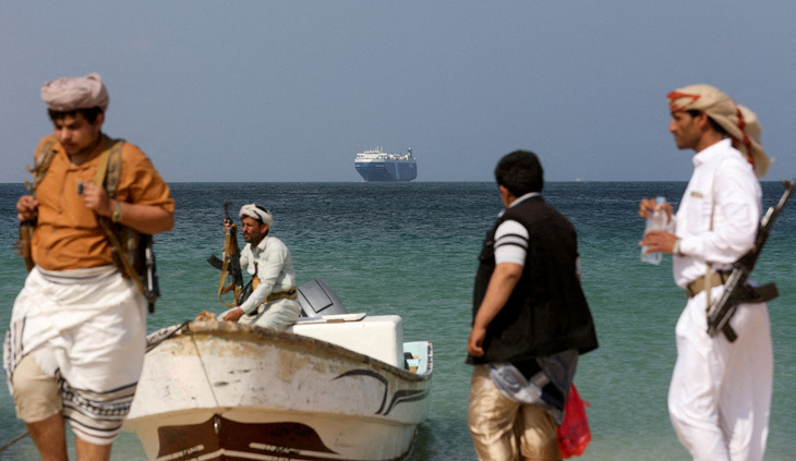 Những người có vũ trang đứng trên bãi biển, còn đằng xa là tàu thương mại Galaxy Leader (do công ty Nhật Bản vận hành và bị nhóm phiến quân Houthi bắt giữ năm ngoái) ngoài khơi bờ biển al-Salif, Yemen vào ngày 5-12-2023 - Ảnh: REUTERS