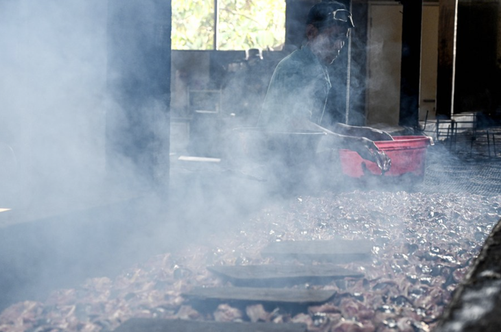 Một công nhân cần mẫn xếp từng lát thịt cá lên vỉ nướng để chúng tiếp xúc với lửa than và khói gỗ thơm. Việc này giúp món ăn trở nên thơm ngon và bảo quản được lâu dài