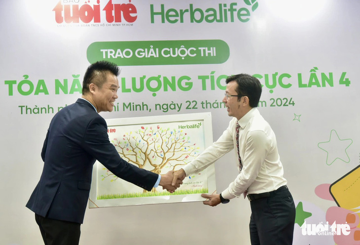 Giám đốc truyền thông Herbalife Việt Nam Nguyễn Thành Đạt (bên trái) nhận bức tranh có dấu vân tay của tất cả khách mời mang thông điệp lan tỏa lối sống tích cực từ tay Phó tổng biên tập báo Tuổi Trẻ Trần Xuân Toàn (bên phải) - Ảnh: T.T.D.