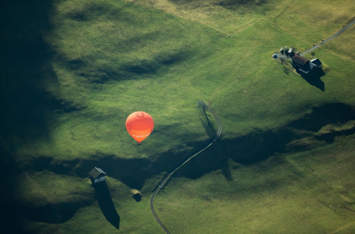 Khung cảnh nhìn trên cao đẹp như tranh vẽ của thị trấn Chateau-d'Oex: một chiếc khinh khí cầu màu cam chậm rãi đi qua đồng cỏ xanh ngát - Ảnh: REUTERS