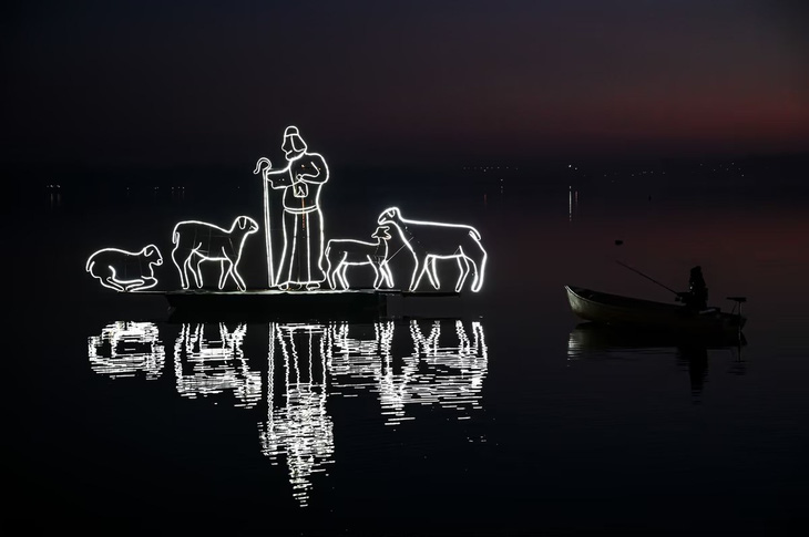 Một người đàn ông ngồi câu cá trên thuyền lúc hoàng hôn bên cạnh tác phẩm nghệ thuật được chiếu sáng đặt trên hồ Pusiano tại Como, Italia vào giữa tháng 12 vừa qua. (Ảnh: Anadolu/Getty)