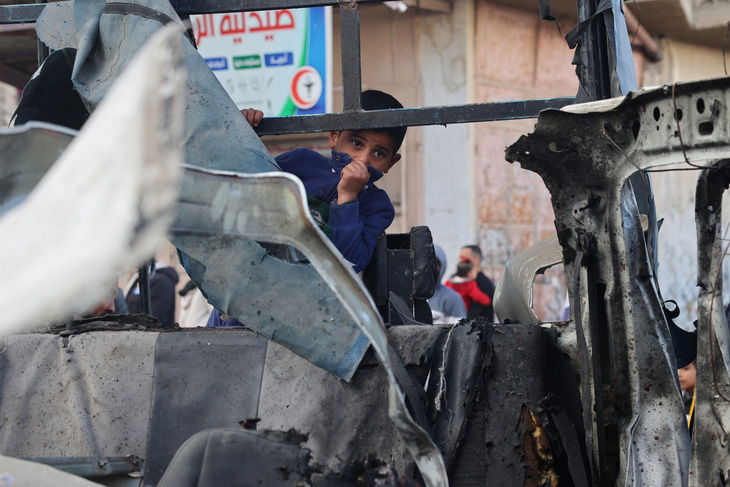 Một cậu bé người Palestine tại hiện trường vụ xe cảnh sát bị phá hủy trong vụ pháo kích của Israel ở TP Rafah, miền nam Gaza - Ảnh: AFP