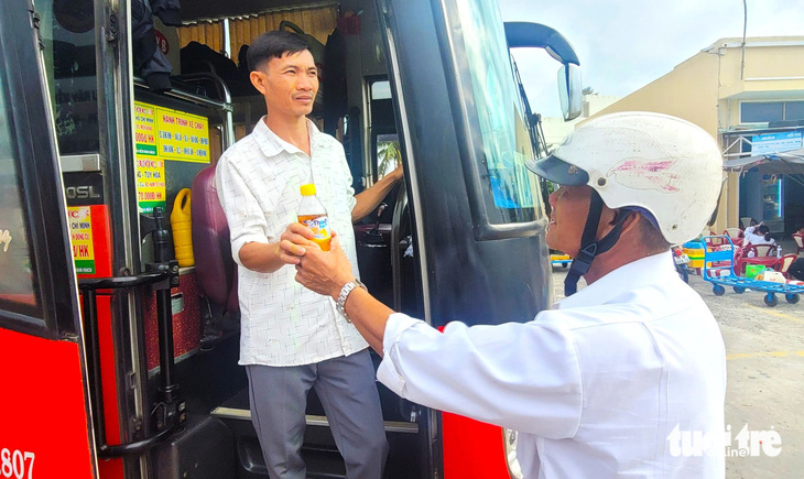 Ông Nguyễn Khoa Nam đưa chai nước cho con trai ở bến xe - Ảnh: NGUYỄN HOÀNG