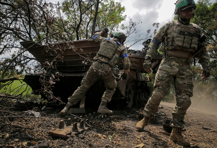 Binh sĩ Ukraine bên xác một xe chiến đấu của Nga - Ảnh: REUTERS