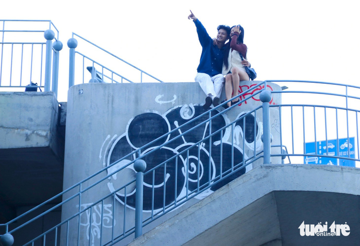 Đôi bạn trẻ chụp hình tại đỉnh cầu thang bộ bị xịt sơn lem luốc hình vẽ kiểu graffiti 