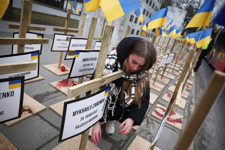 Người phụ nữ Ba Lan bên cạnh quốc kỳ Ukraine, thập giá, được bày biện trước Đại sứ quán Nga ở Warsaw, ngày 24-2 - Ảnh: REUTERS
