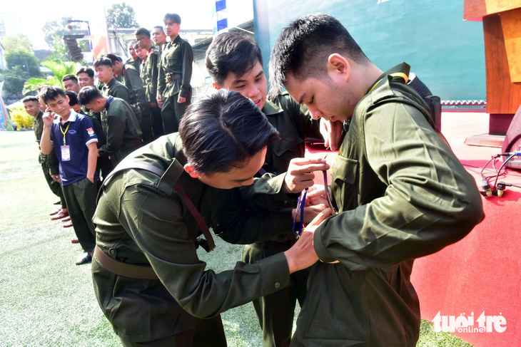 Trại viên Đinh Quốc Trung (giữa) chỉnh cảnh phục cho đồng đội mới, khi các trại viên/thanh niên trúng tuyển nghĩa vụ công an của 10 phường trong quận 1 chuẩn bị chụp ảnh lưu niệm toàn đội