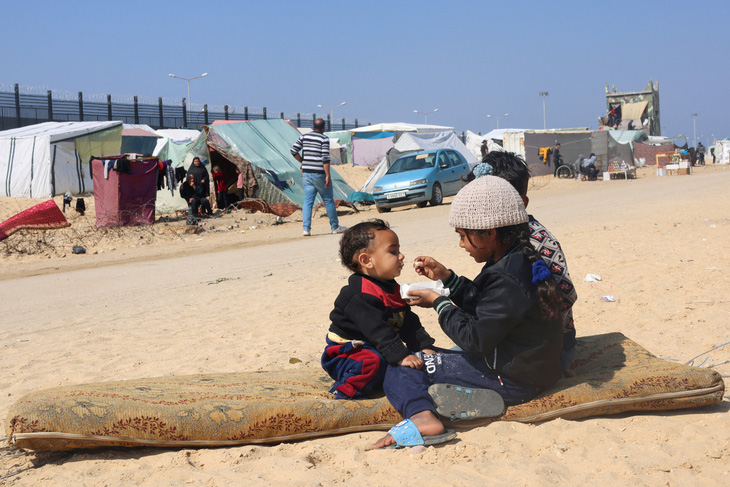Bé gái Palestine cho em trai ăn tại khu lều trại ở thành phố Rafah, nằm ở phía nam Dải Gaza và giáp biên với Ai Cập, hôm 25-2. Cơ quan y tế Gaza ngày 26-2 cho biết có ít nhất 29.782 người ở Gaza đã thiệt mạng kể từ 7-10. Ảnh: Reuters