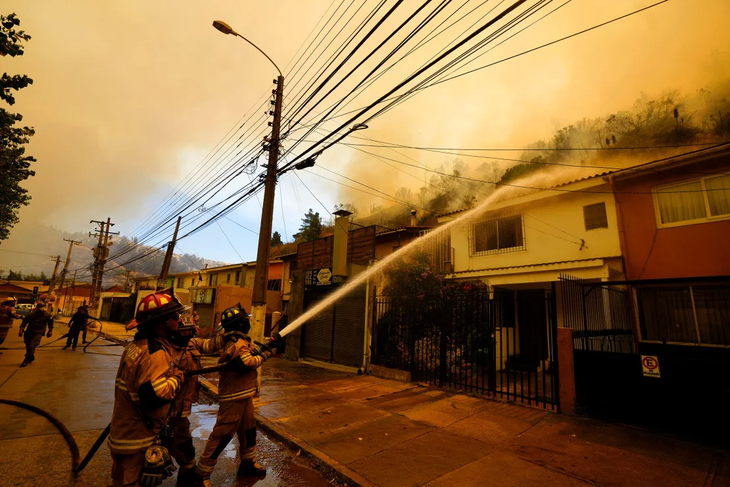 Lính cứu hỏa phun nước bảo vệ các ngôi nhà khi đám cháy rừng bùng phát gần đó - Ảnh: Esteban Felix/AP