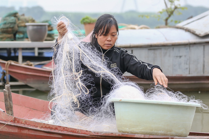 Chị Hiếu, một ngư phủ dạn dày kinh nghiệm, tranh thủ đan lại tấm lưới đánh cá bị rách hôm trước - Ảnh: HÀ QUÂN