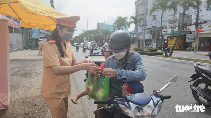 Lực lượng cánh sát giao thông Công an tỉnh An Giang phát nước suối và sữa cho 4 mẹ con chị Nhung - Ảnh: BỬU ĐẤU