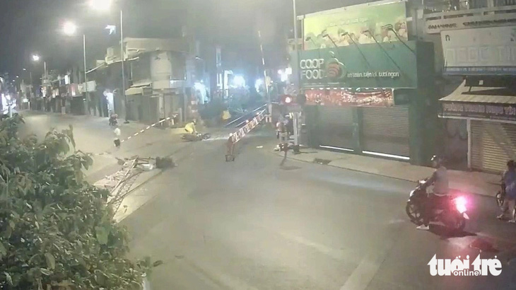Người đi xe máy với tốc độ nhanh đã tông vào chắn trên đường Nguyễn Kiệm, quận Phú Nhuận, TP.HCM. Xe máy văng vào đường ray. Một nhân viên đường sắt phải kéo xe máy ra khỏi đường ray, nhân viên còn lại phải chạy đi ra tín hiệu dừng tàu khẩn cấp - Ảnh: Cắt từ camera