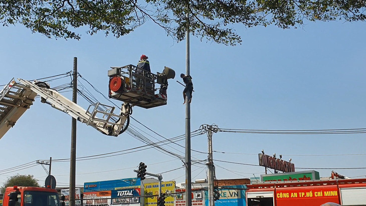 Cảnh sát dùng xe thang tiếp cận nam thanh niên đang cố thủ trên cột đèn - Ảnh: B.H.