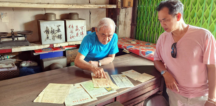 Ông Kha Minh (trái), thân nhân bà Kha Quyên ở quán trà Ô Tòng Ký, cùng anh La Hưng xem các hóa đơn, biên lai các tiệm vàng xưa trên đường Phan Chu Trinh sát chợ Bến Thành Ảnh: Phúc Tiến chụp sáng 20-3-2024