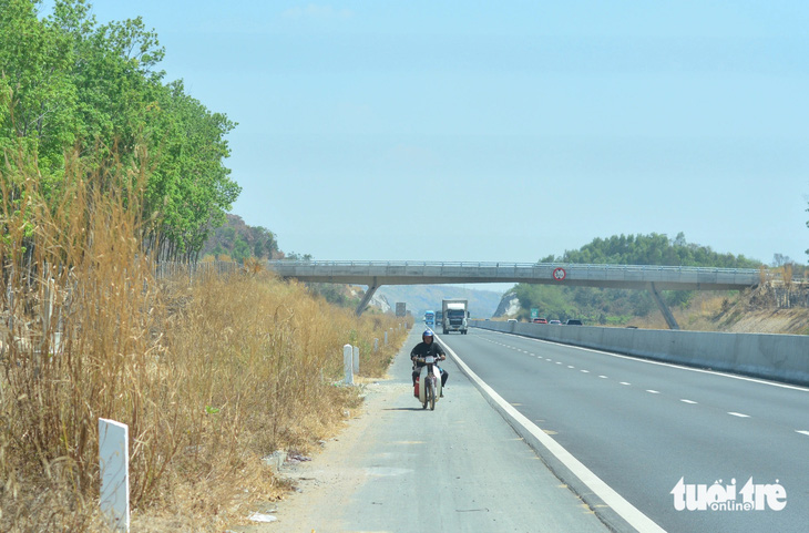 Một người đàn ông chạy xe máy chui qua đoạn hàng rào dân sinh chưa hoàn thiện để đi vào cao tốc Phan Thiết - Dầu Giây, đoạn gần cột mốc Km48 bên phải tuyến.