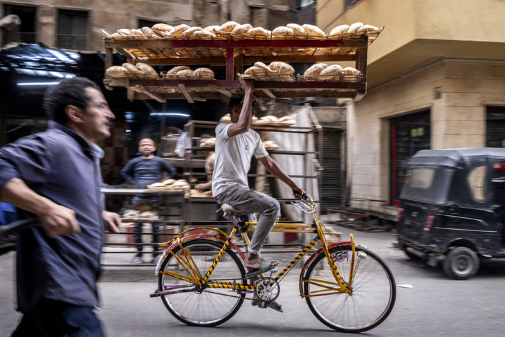 Người đàn ông đạp xe mang theo khay bánh mì khổng lồ như làm xiếc giữa đường phố thủ đô Cairo, Ai Cập ngày 6-3 - Ảnh: AFP