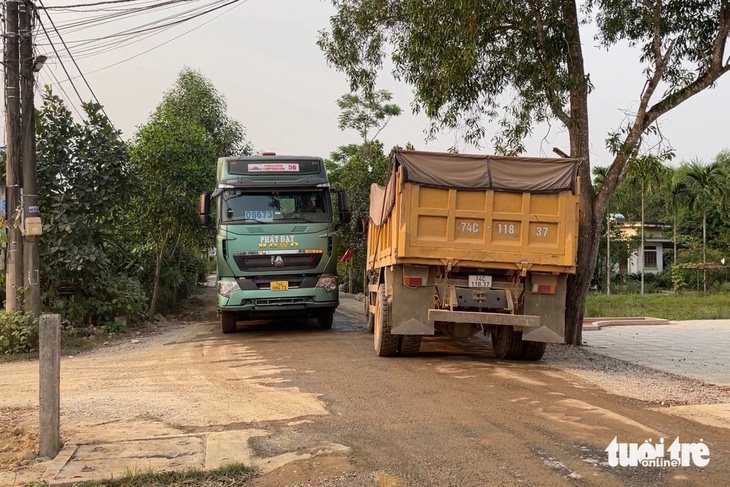 Hai xe tải lớn tránh nhau trên đường làng chật hẹp khiến người dân không thể đi lại - Ảnh: HOÀNG TÁO