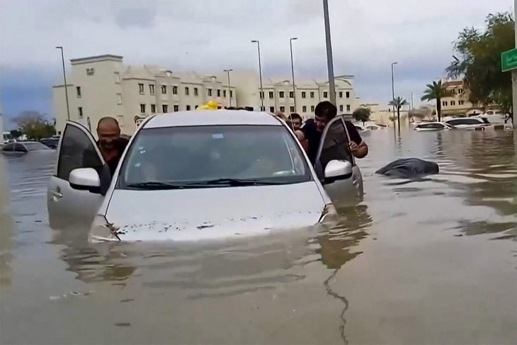 Người dân cố gắng đẩy một chiếc ô tô bị mắc kẹt do lũ lụt bất thường ở Dubai hôm 16-4 - Ảnh: AFP