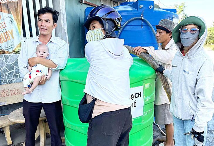 Chị Kim (đội mũ bảo hiểm) trực tiếp bơm nước vào bồn chứa giúp người dân - Ảnh: TRÚC QUYÊN