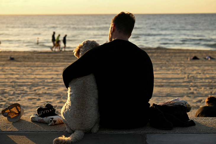 Một người đàn ông quàng tay ôm con chó của mình khi ngồi trên bãi biển ở Coogee tại thành phố Sydney, bang New South Wales, Úc vào ngày 25-4 - ẢNH: REUTERS