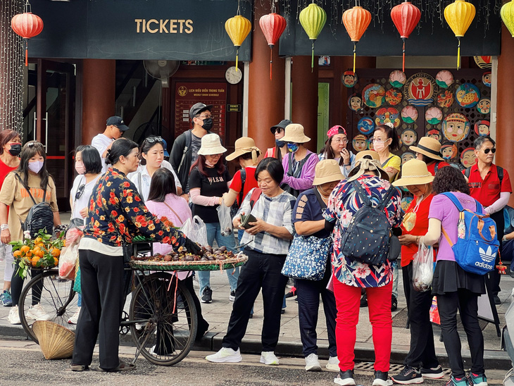 Một nhóm du khách mua hoa quả tại xe hàng rong trên phố Đinh Tiên Hoàng (quận Hoàn Kiếm) sáng 13-5 - Ảnh: PHẠM TUẤN