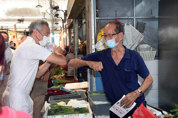 Thủ tướng Lý Hiển Long giao lưu cùng tiểu thương tại một khu chợ ở Singapore, với một cú chạm khuỷu tay thay cho lời chào trong bối cảnh COVID-19 - Ảnh: MCI