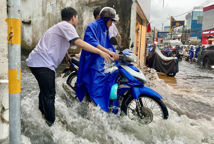 Nước chảy như thác tại hẻm đường Võ Văn Ngân (TP Thủ Đức) khiến nhiều xe máy té ngã. Các bạn học sinh trường gần đó ra hỗ trợ người dân - Ảnh: CHÂU TUẤN