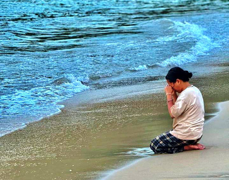 Chị T. - mẹ của cháu bé L.P.N. - quỳ bên bãi biển, ngóng vọng tin con sau khi cháu bé mất tích - Ảnh: Đội xe cấp cứu 0 đồng