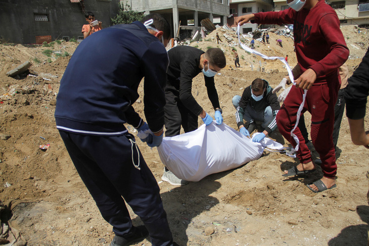 Người Palestine bên cạnh một thi thể được chôn trong ngôi mộ tập thể ở phía bắc Dải Gaza hôm 15-4 - Ảnh: REUTERS