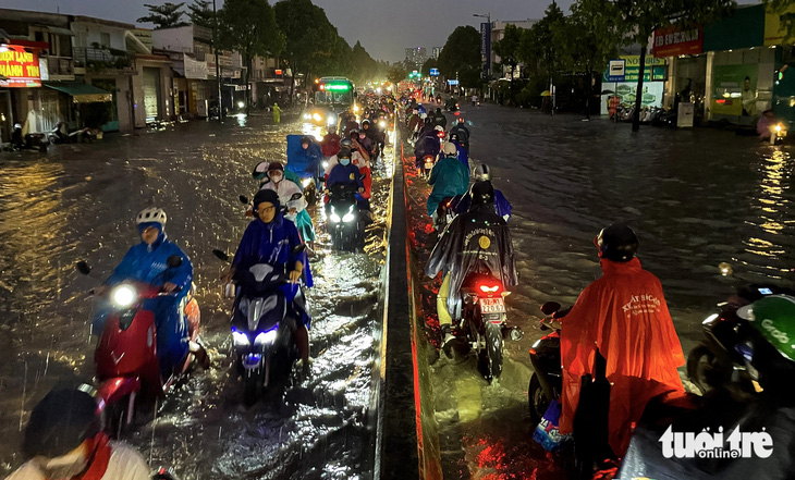 Mưa kèm theo nước từ con rạch gần đó gây ngập đường Phạm Văn Đồng, một số người đi xe máy cố gắng chạy sát vào tim đường để đi - Ảnh: CHÂU TUẤN