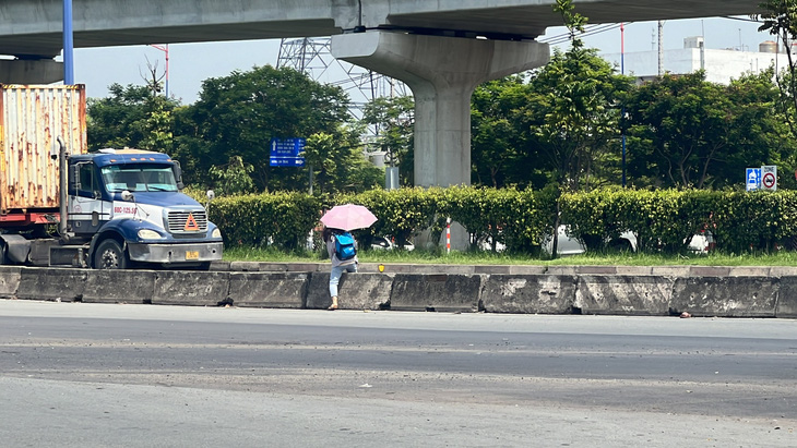 Nữ sinh vừa che dù vừa băng qua trước đầu xe container trên xa lộ Hà Nội, TP Thủ Đức - Ảnh: XUÂN ĐOÀN