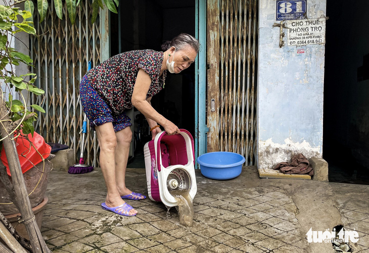 Trưa 21-5, bà Trần Thị Tuyết Nhâm (87 tuổi) múc từng xô nước cống tràn từ đường 38 vào nhà - Ảnh: CHÂU TUẤN