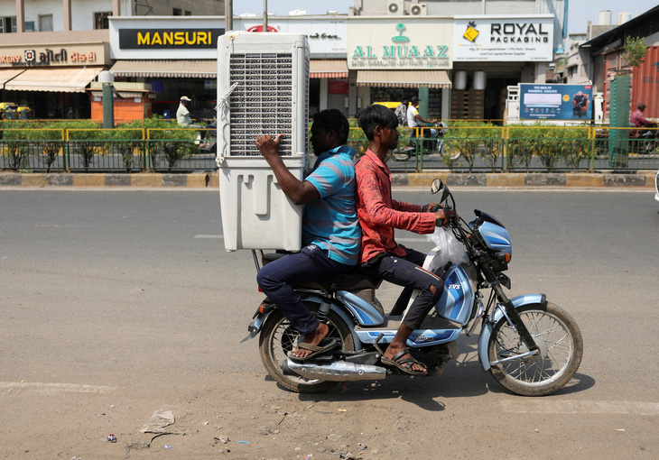 Giữa cái nắng hè gay gắt tại TP. Ahmedabad, bang Gujarat, Ấn Độ, hai người đàn ông chở nhau bằng xe máy để vận chuyển một chiếc máy làm mát không khí về nhà - Ảnh: REUTERS