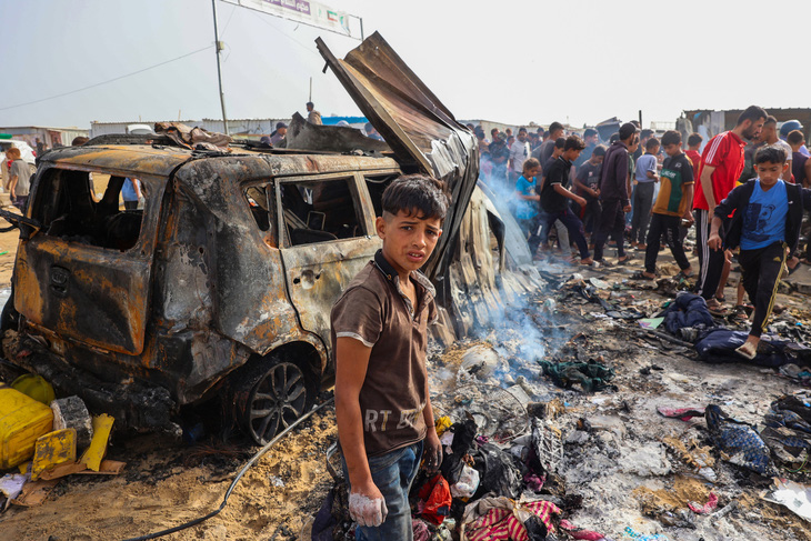 Cậu bé người Palestine đứng trước một chiếc xe bị phá hủy do trận không kích nhầm của quân đội Israel vào một trại tị nạn ở Rafah - Ảnh: AFP