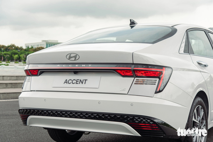 Hyundai Accent 2024 có phần đuôi hơi vuốt xuống kiểu Fastback, trông trở nên thể thao và trẻ trung hơn. Cụm đèn hậu LED kéo dài sang hai bên dạng chữ H. Cản sau có 4 cảm biến và camera lùi. Cốp xe vẫn chỉ đóng/mở cơ, nhưng tích hợp tính năng mở cốp rảnh tay (Smart trunk) rất hữu dụng khi xách đồ. 