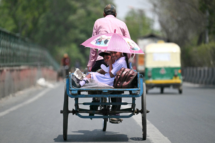 Hai đứa trẻ cười tươi dưới ô khi di chuyển trên xe ba bánh, giữa thời tiết mùa hè nắng gắt ở thủ đô New Delhi, Ấn Độ vào ngày 2-5 - Ảnh: AFP