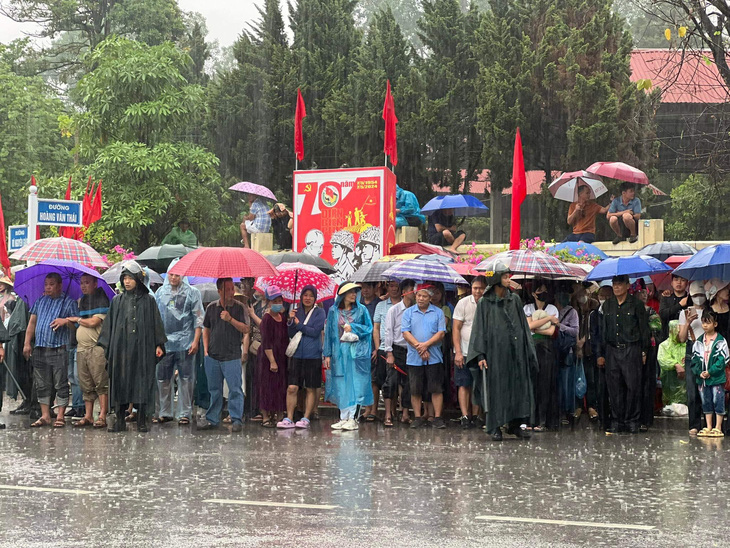 Dù cơn mưa lớn trút xuống nhưng người dân vẫn giữ nguyên vị trí khi nhớ về 56 ngày đêm "khoét núi ngủ hầm mưa dầm cơm vắt" của các chiến sĩ Điện Biên năm xưa - Ảnh: NAM TRẦN