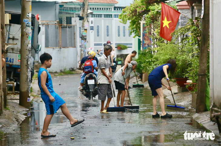 Người dân tại các con hẻm lân cận hì hục dọn rác, đẩy nước từ rạch tràn lên - Ảnh: CHÂU TUẤN