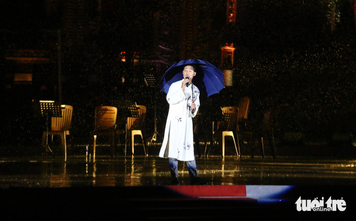 Ca sĩ Đức Tuấn đội mưa hát bài Nắng thủy tinh trong đêm nhạc Trịnh Công Sơn ở Huế tối 9-6 - Ảnh: NHẬT LINH