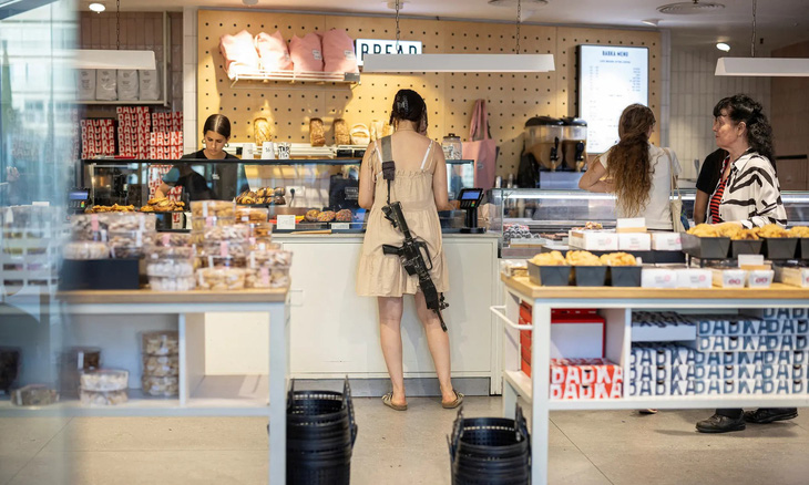 Một phụ nữ khoác theo khẩu súng trường khi đi vào mua hàng ở một tiệm bánh tại thành phố Tel Aviv của Israel. (Marko Djurica/Reuters)