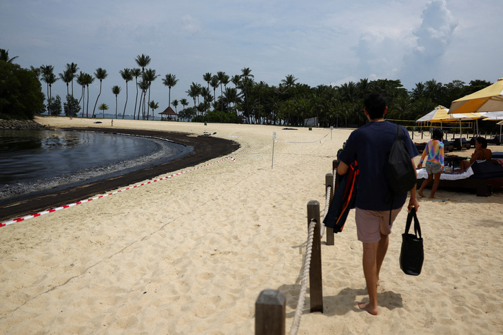 Một người đàn ông đi bộ gần biển báo và dây băng tại nơi có dầu loang ở bãi biển Tanjong, Sentosa, Singapore ngày 15-6 - Ảnh: REUTERS