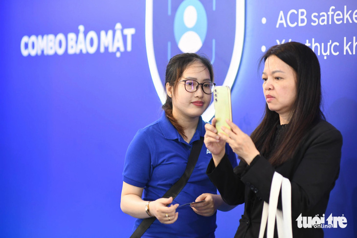 Chị Thùy Vân (trái) chăm chú làm theo hướng dẫn của nhân viên ACB để xác thực khuôn mặt, tăng cường đảm bảo an toàn trong tài khoản - Ảnh: QUANG ĐỊNH