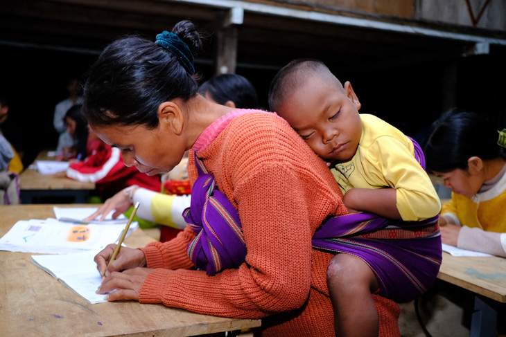 Chị Đương (41 tuổi) cặm cụi rèn chữ viết trong khi cậu con trai 4 tuổi đang ngủ trên địu - Ảnh: T.LỰC