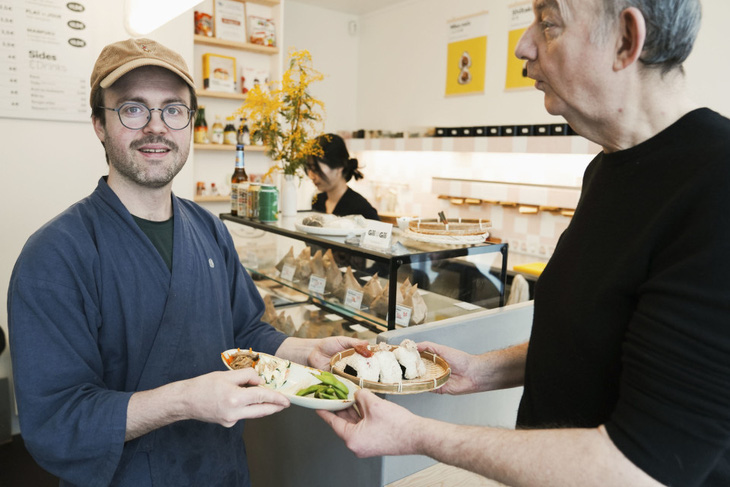 Anh Samuel Trifot, chủ một cửa hàng cơm nắm (trái), đưa phần cơm cho thực khách của mình - Ảnh: Kyodo News